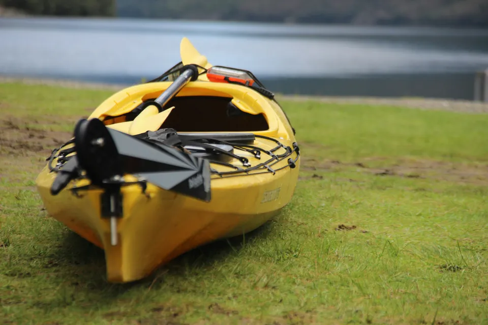 Close view of a yellow kayak on grass with a folding two-wheel cart, a paddle and a small dry box strapped across its deck.