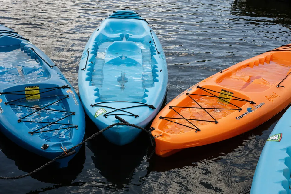 Four sit-on-top kayaks in blue, light blue and orange tied together on dark, calm water, seen from above.